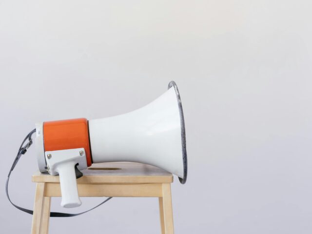 Close-up of a megaphone resting on a wooden chair with a minimalist background.