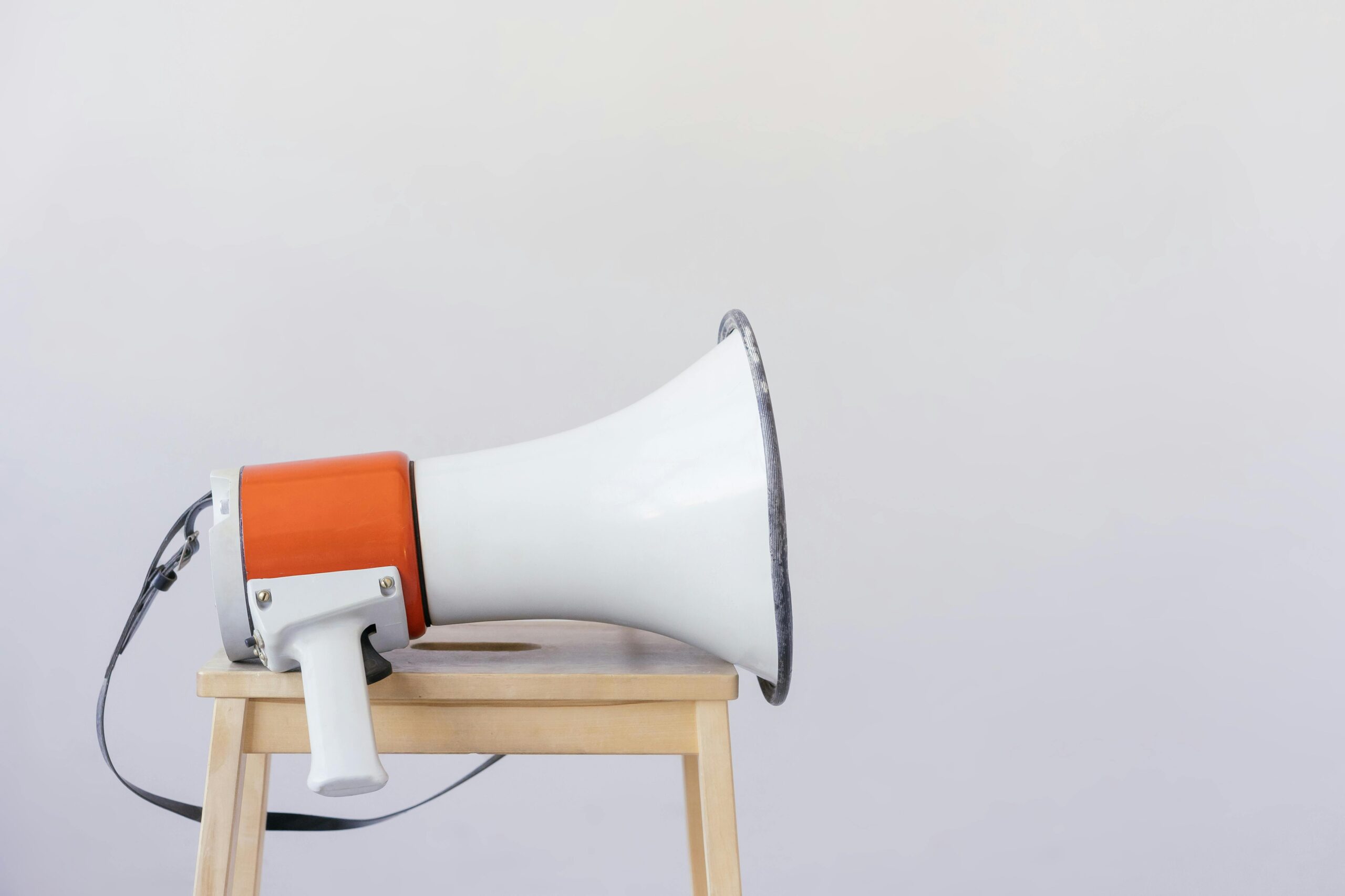 Close-up of a megaphone resting on a wooden chair with a minimalist background.